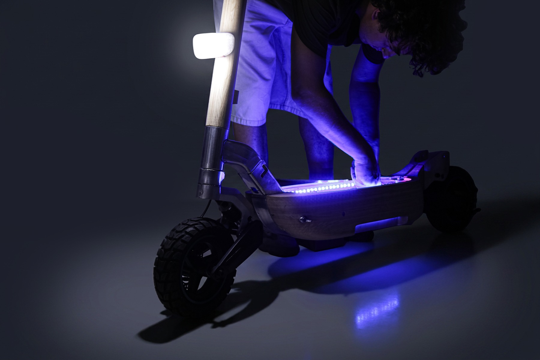 Person adjusting the scooter's underside lighting in a dark studio, purple glow