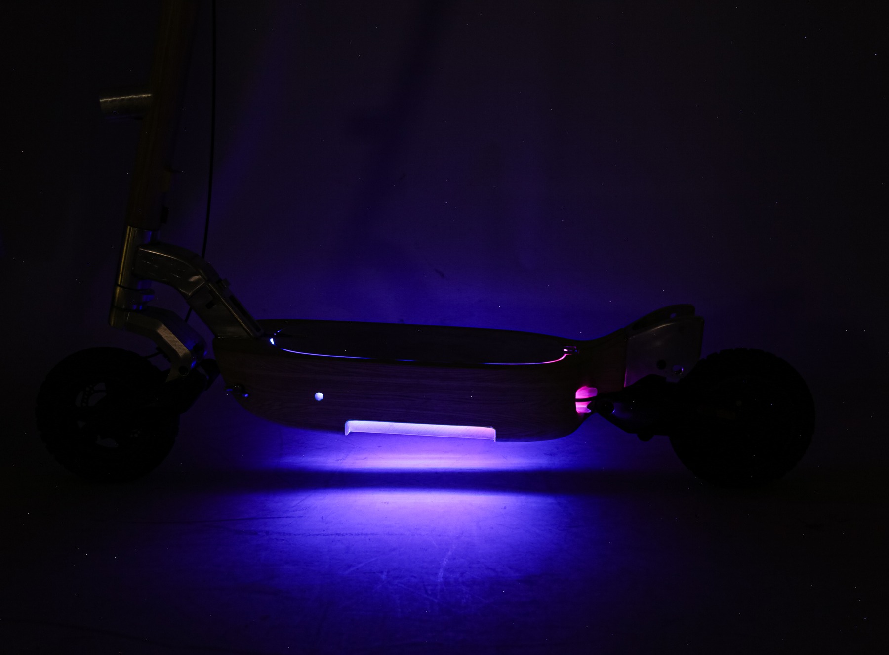 Wide shot of the scooter's underside light glowing purple in a dark studio