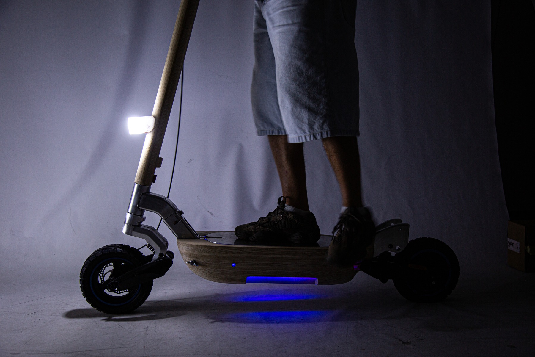 Person standing on the scooter in a dark studio, underside light glowing
