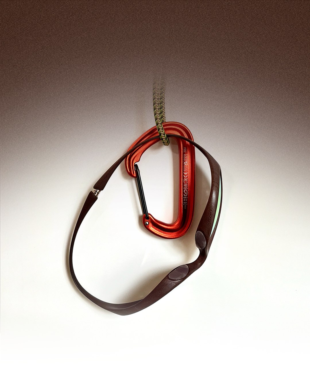 Orange carabiner clipped through a brown leather eyewear strap, studio gradient background