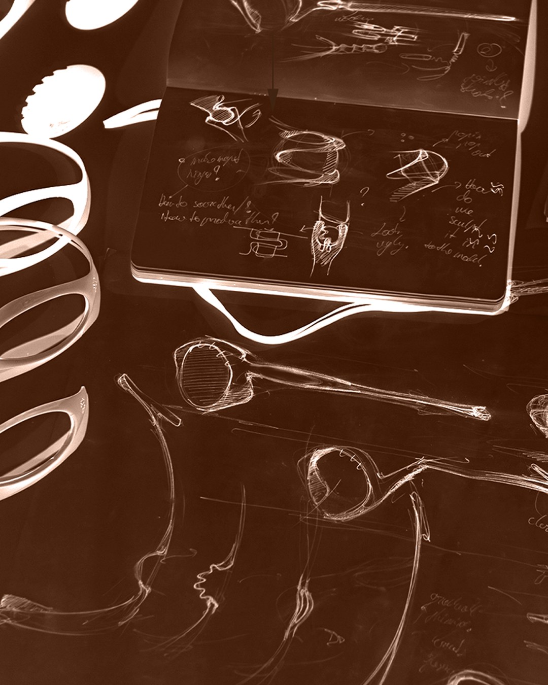 Sepia-toned photo of a sketchbook with hand-drawn hinge studies and coiled wire mockups